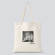 A white tote bag with a black and white hand crafted stamp design of an airplane on the Mad Rock logo with Allison Vest's signature below.