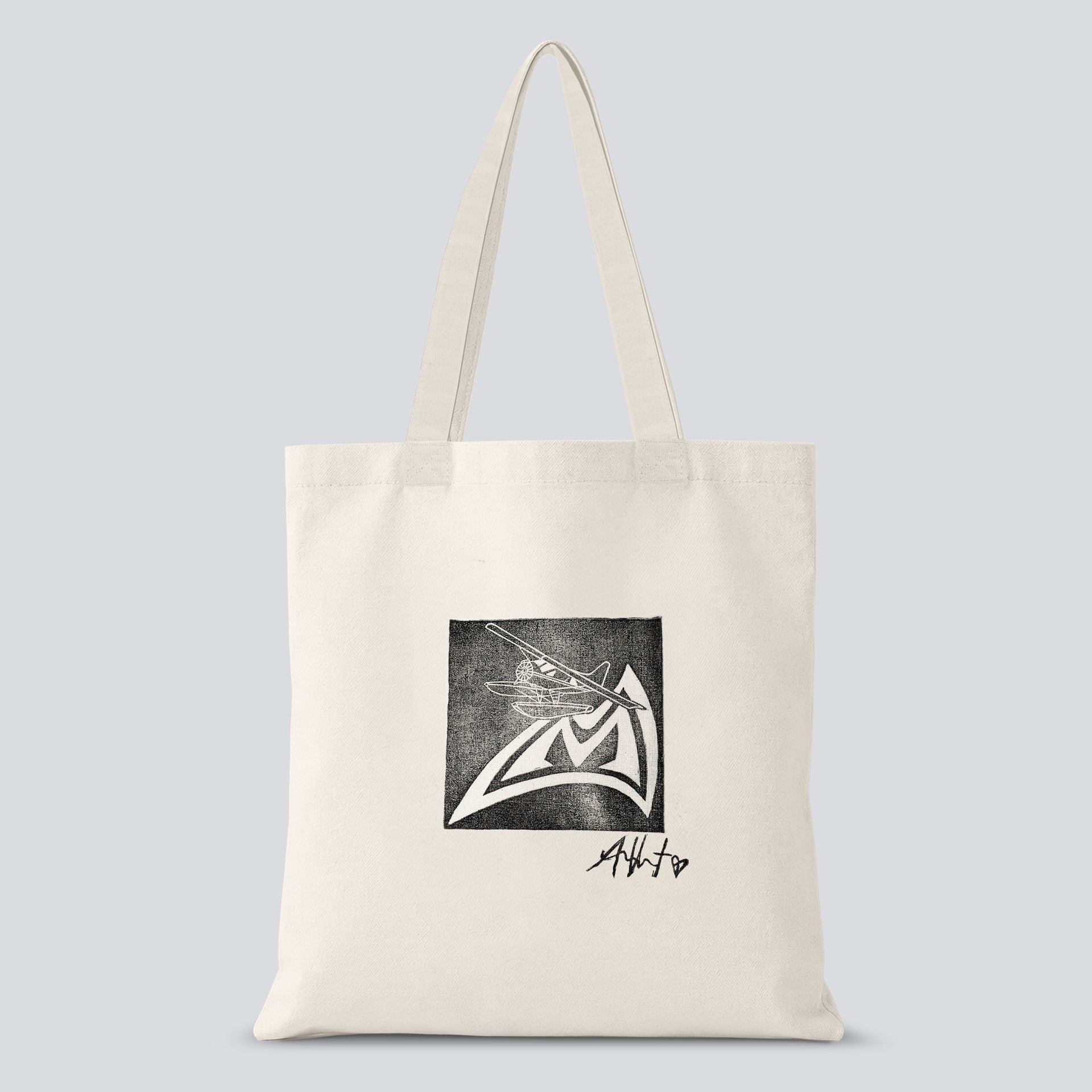 A white tote bag with a black and white hand crafted stamp design of an airplane on the Mad Rock logo with Allison Vest's signature below.