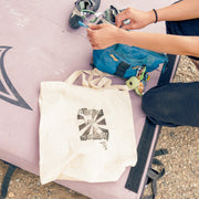 Person sitting on a pink mat with a white tote bag, blue bag, and climbing shoes.