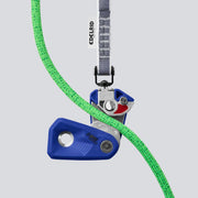 An open blue climbing belay device with green rope on a light gray background
