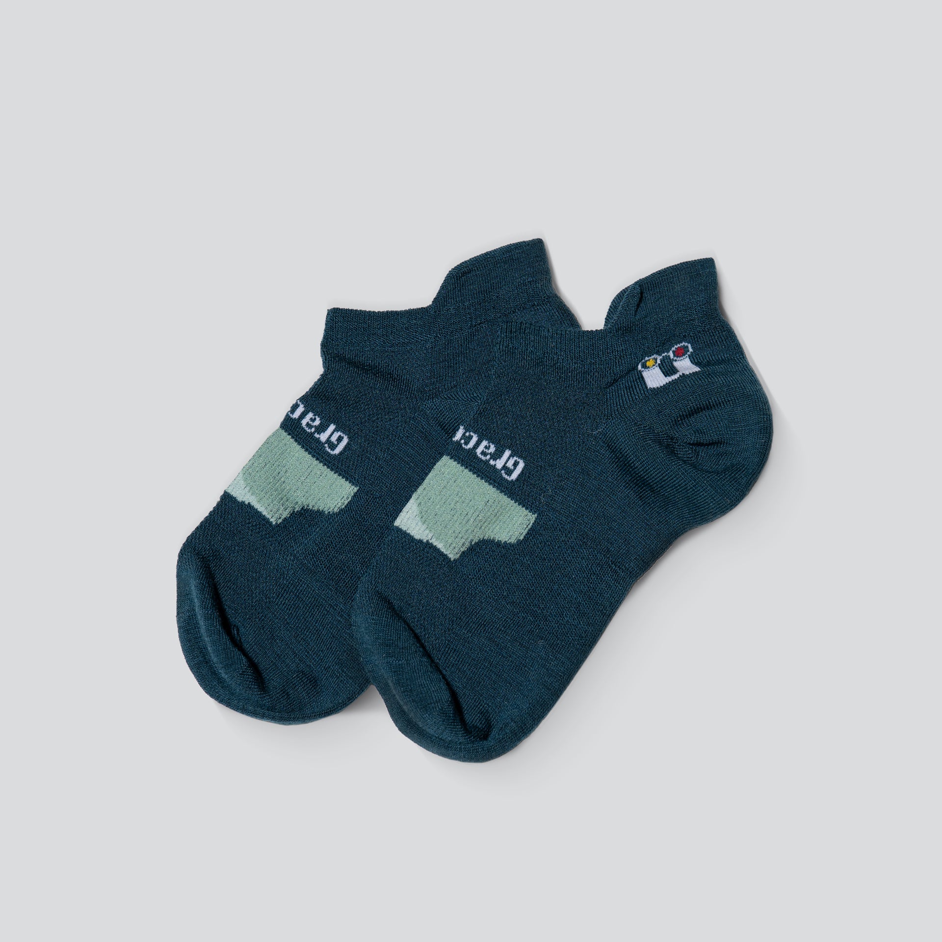 A pair of ankle socks in dark teal, featuring a light mint green arch support panel on the sole and a small white and blue logo on the side.