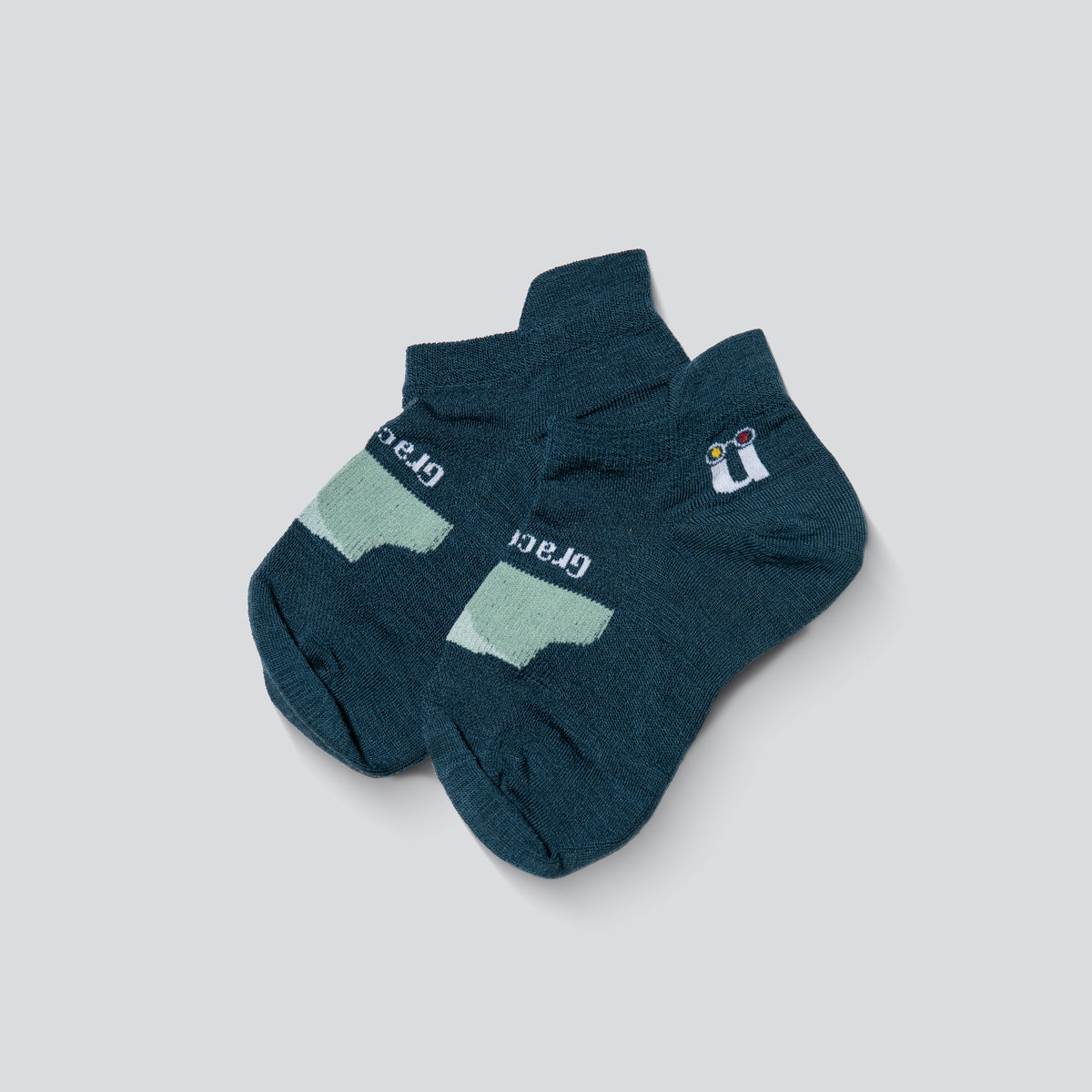 A pair of ankle socks in dark teal, featuring a light mint green arch support panel on the sole and a small white and blue logo on the side.