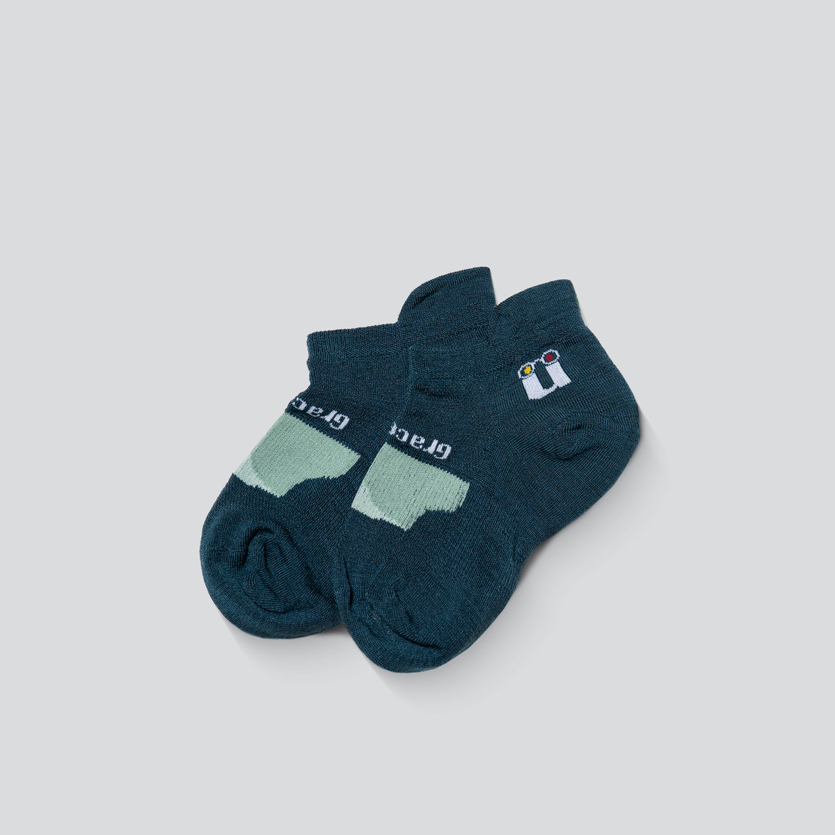 A pair of ankle socks in dark teal, featuring a light mint green arch support panel on the sole and a small white and blue logo on the side.