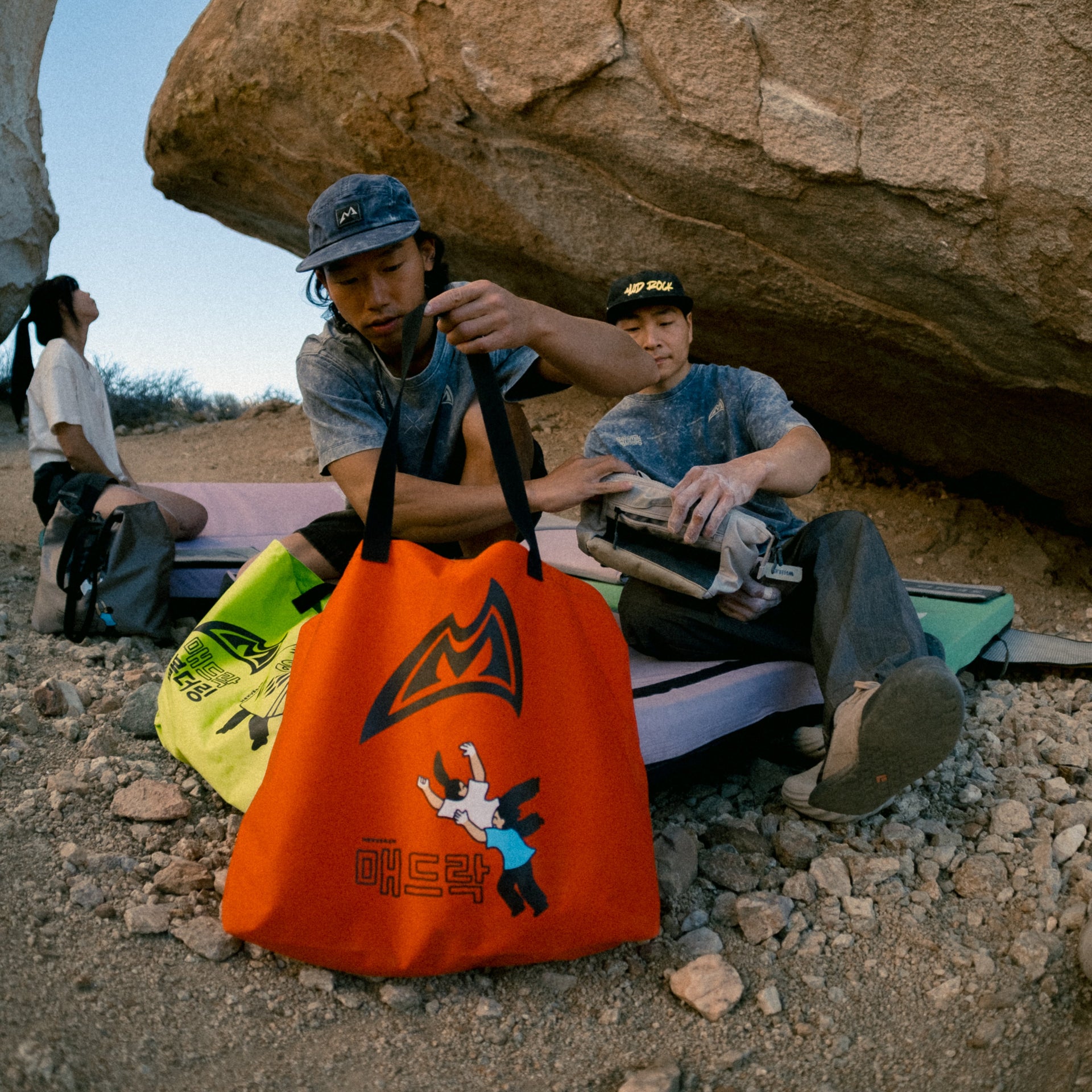 3 climbers sitting near a rock with tote bags in the foreground