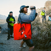 a climber smiling and holding a camcorder with a tote bag over their shoulder