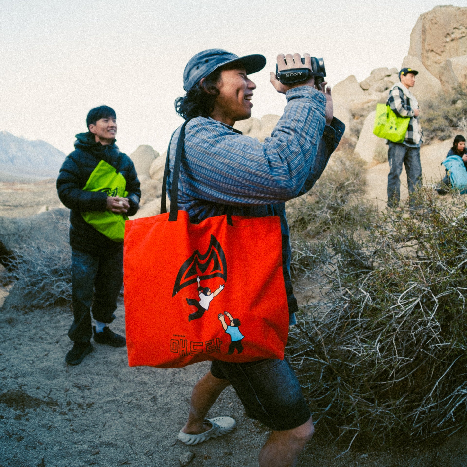 a climber smiling and holding a camcorder with a tote bag over their shoulder