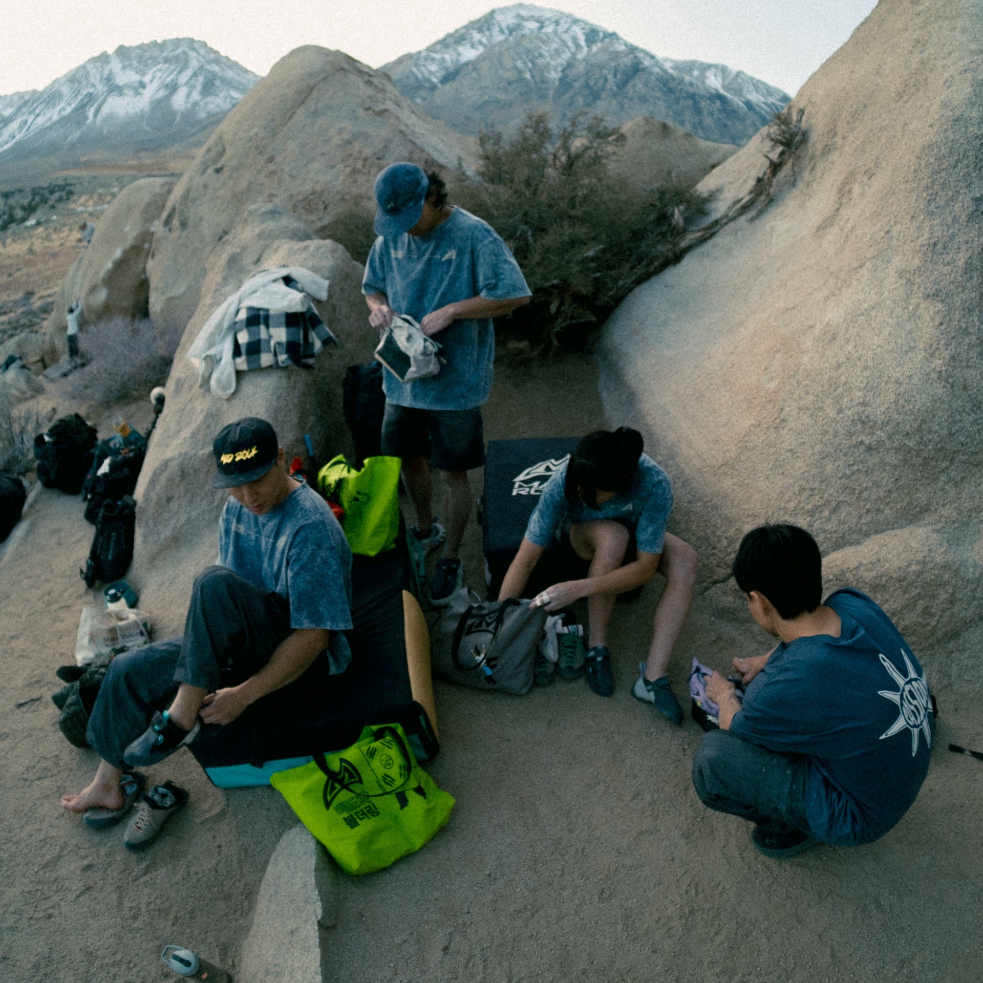 a group of climbers getting ready to climb with climbing gear on the ground and tote bags present