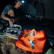 1 climber crouching near a crash pad at night with a tote bag in the foreground