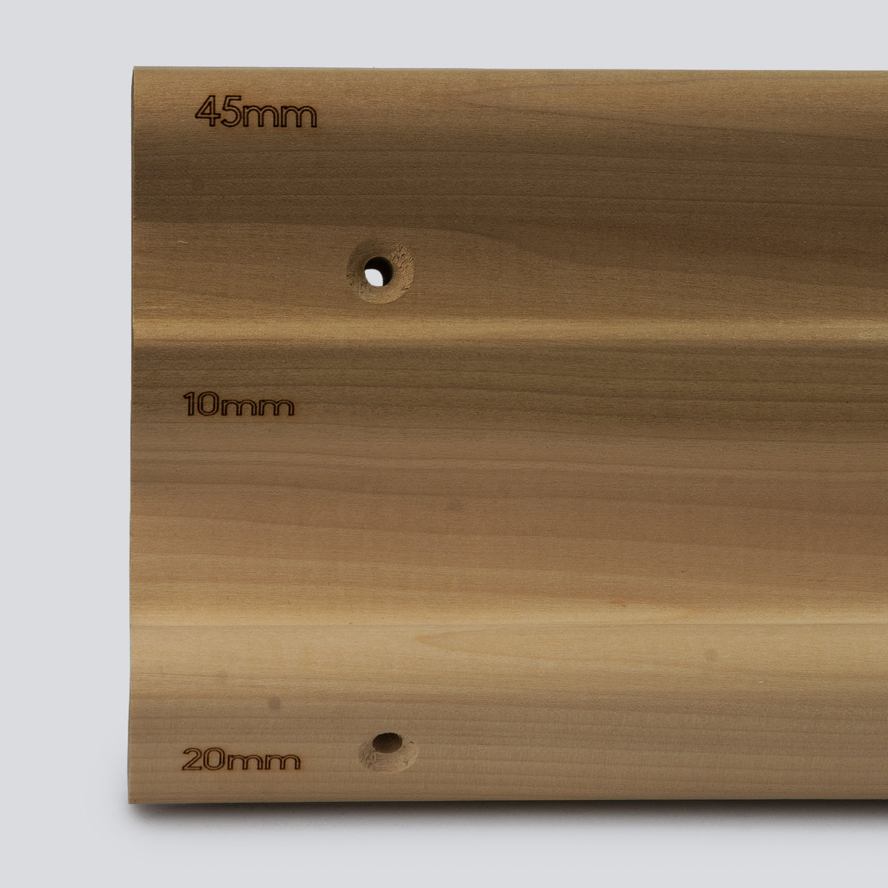A close up of a wooden hangboard with 3 different edges on a grey background