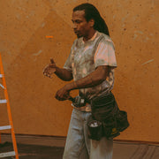 athlete Mickael Mawem wearing an acid wash shirt with a drill in hand and a tool belt around his waist