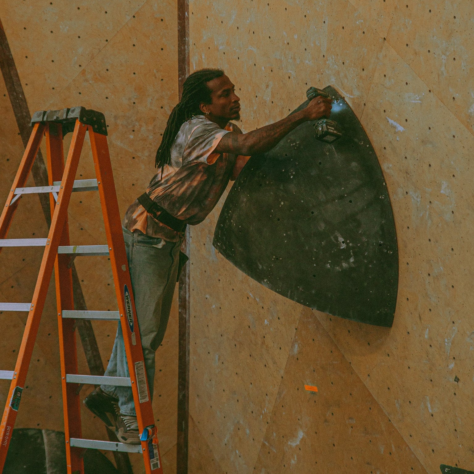 athlete Mickael Mawem wearing an acid wash shirt and drilling a large volume into a wall